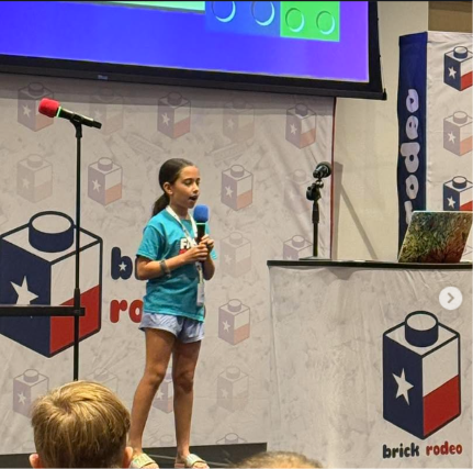 Sloane, age 10, on stage at Brick Rodeo in Austin holding a microphone and presenting Fast Brix! in front of a Brick Rodeo backdrop.